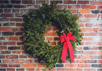 evergreen wreath dressed with a single red ribbon hanging on a red brick wall