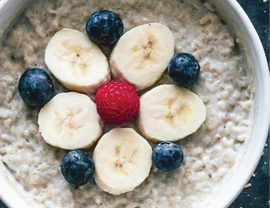 close up photo of bowl of oatmeal decorated with slices of banana blueberries and a red raspberry