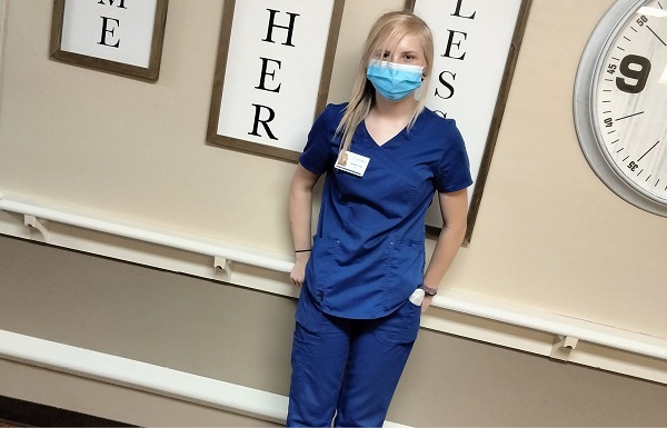 young lady named Autumn wearing blue scrubs standing against wall at Franklin Simpson Nursing and Rehab