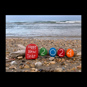 happy new year 2024 drawn on colored rocks, sitting on the shore of a beach.